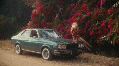 Sarışın Beyaz Kadın, Teal Classic Car 'ın kaputuna tünemiş, Çiçekli Çitlere Karşı Gevşek Poz, Editör