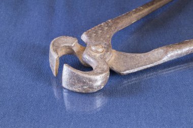 Paslı pense yansıması olan bir masada yatıyor. Mavi arkaplanda marangoz aracı