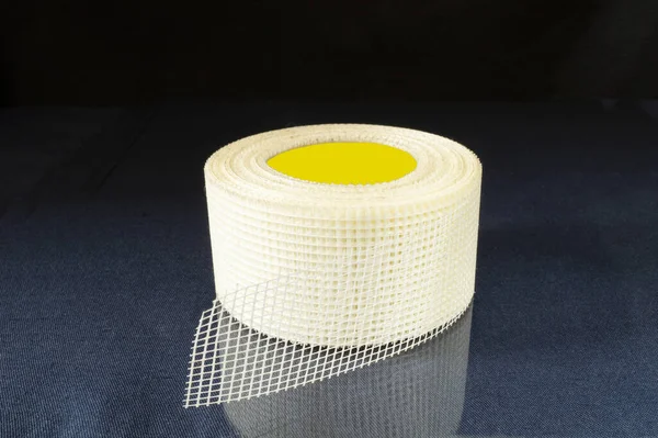 Masanın üzerinde bir rulo yapışkan ağ yansıması var. Siyah arka planda endüstriyel nesneler.