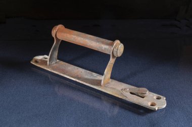 Paslı kapı tokmağı masanın üstünde. Siyah zemin üzerinde demir bir nesne