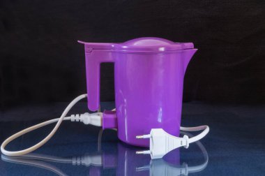 Cam bir masada yansıması olan elektrikli bir çaydanlık. Siyah arkaplanda mutfak aleti