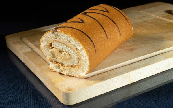 Mutfaktaki ahşap bir tahtanın üzerinde tatlı bir rulo. Gıda ürünleri siyah arka planda