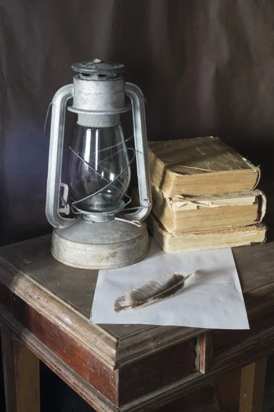 Lâmpada de querosina envelhecida com livro e pena para descansar sobre ta de madeira — Fotografia de Stock