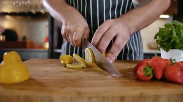 Крупный план Man Cook Cuts Fresh Fruits Lemon and Strawberry on Wooden Cutting Board — стоковое видео