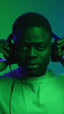 Siyah adamın portresi kulaklık takıyor ve Neon Light of Inside Shot 'da izole edilmiş müzik dinliyor. Bir Afrikalı İşiten İnternet Oyuncusunun Sesi. Telefon Teknolojisinde Amerikan Model Pozisyonu