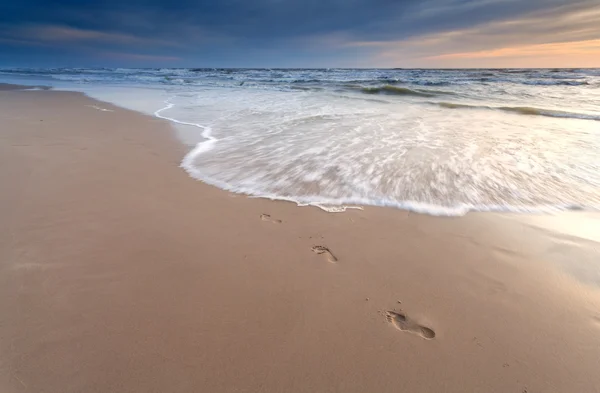 Huellas de pies en la playa de arena al atardecer — Foto de Stock