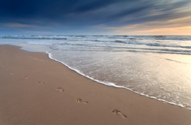 foot prints on sand beach at sunset clipart