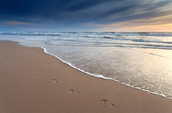 Odbitki stóp na piasku plaży o zachodzie słońca — Zdjęcie stockowe