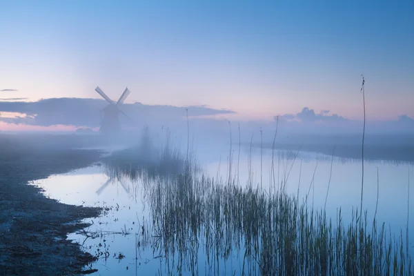 Větrný mlýn u řeky v mlhavé šero — Stock fotografie
