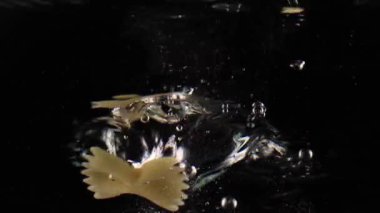 Geleneksel İtalyan mutfağı ağır çekimde farfalle makarnası suya düşüyor siyah arka planda uçan kelebekler gibi.