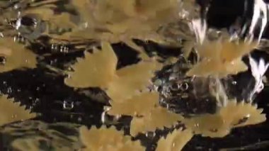 Geleneksel İtalyan mutfağı ağır çekimde farfalle makarnası suya düşüyor siyah arka planda uçan kelebekler gibi.