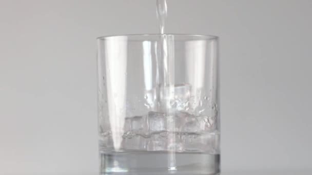 Наливаємо воду в склянку з льодом на білому фоні — стокове відео
