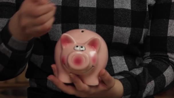 小猪银行的业务站在一堆硬币的概念。一只手正在把一枚硬币放在一个生活方式的储蓄罐里。省钱是对未来的一种投资. — 图库视频影像