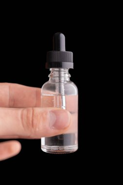 Bir erkek eli siyah arka planda pipetle şişeyi tutuyor.