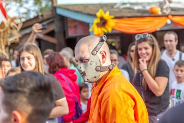 Renkli kıyafetler giymiş, insanlar arasında dolaşan bir psikopatın temsili.