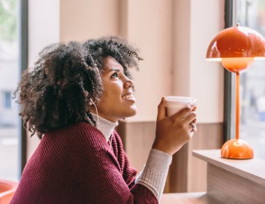Güzel afro kadın soğuk bir günde kahvesini yudumlarken gülümser.