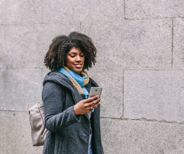 Şirin Afrikalı Amerikalı kız şehirde yürürken cep telefonuna bakarak gülümsedi.
