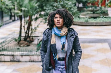 Soğuk bir kış gününde zarif giysiler içinde esmer bir kadın yürür ve yukarı bakar.