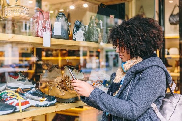 Привлекательная деловая женщина с афроволосами смотрит на свой мобильный телефон перед витриной магазина