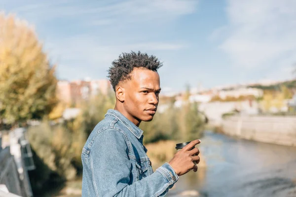 Afro hair man drinks a coffee relaxing in a park in a summer day