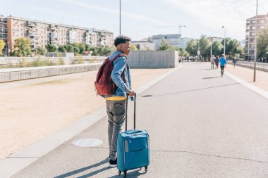 Bavulları ve sırt çantasıyla gezgin yazın bir şehirde yürür.