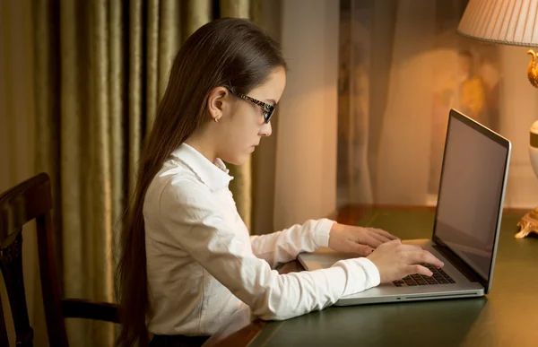 Flicka i skoluniform sitter bakom bordet och använder bärbar dator på — Stockfoto