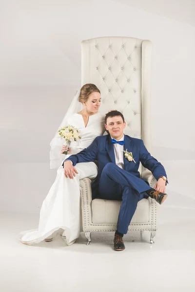 Elegante bruid en bruidegom poseren op stoel in studio — Stockfoto