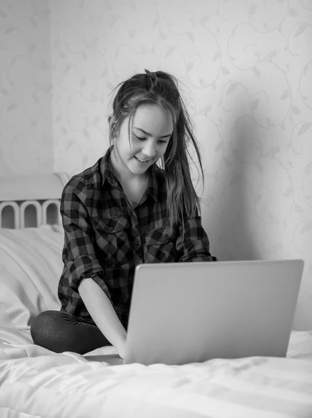 Svart och vitt skott av tonårig flicka sitter på sängen och använda la — Stockfoto