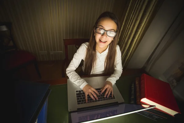 Lächelndes Schulmädchen mit Brille, das bei Dunkelheit am Computer arbeitet — Stockfoto