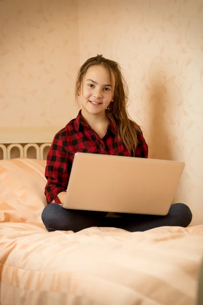 Chica de camisa sentada en la cama en el dormitorio con el ordenador portátil —  Fotos de Stock