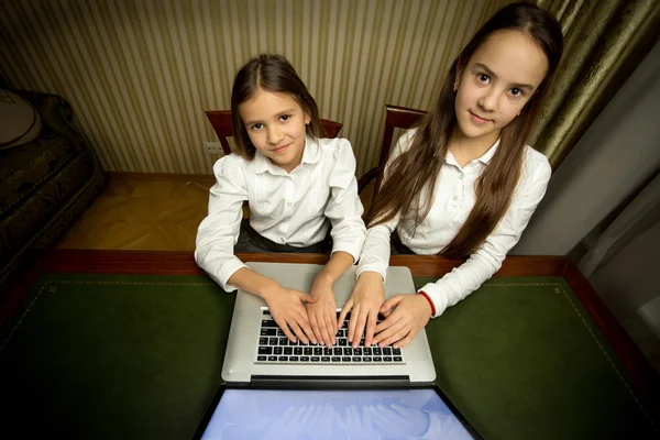 Retrato de dos niñas utilizando el ordenador portátil en el gabinete —  Fotos de Stock