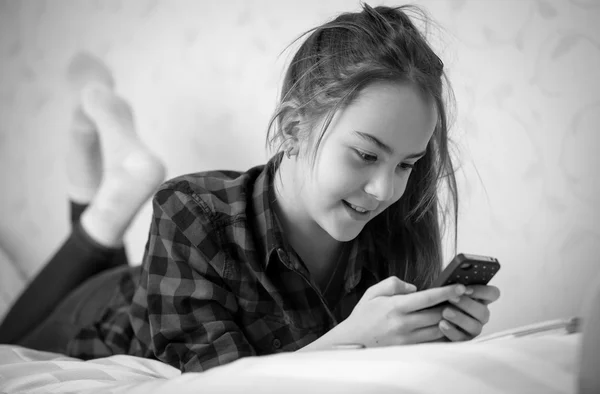 Чорно-білий портрет дівчини-підлітка, що лежить на ліжку і друкує — стокове фото