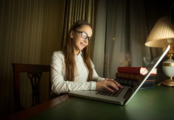 Cute schoolgirl in white shirt doing homework at laptop in dark — Stock Photo, Image