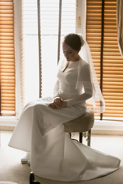 Junge Braut posiert auf Stuhl gegen großes Fenster im Hotelzimmer — Stockfoto