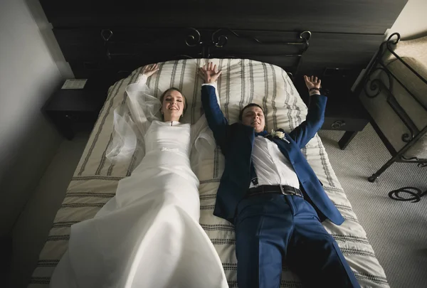 Happy bride and groom lying on bed at hotel room — Stock Photo, Image