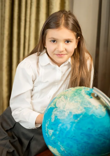 Smiling schoolgirl posing with Earth globe at cabinet — Stock Photo, Image