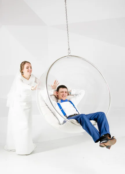 Funny shot of bride swinging groom sitting on bubble chair at st — Stock Photo, Image