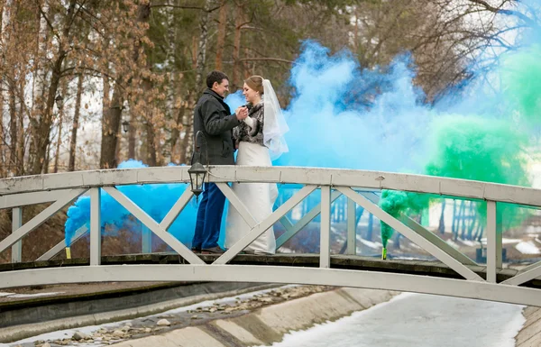 Blue and green smoke covering newlywed couple dancing on bridge — Stock Photo, Image