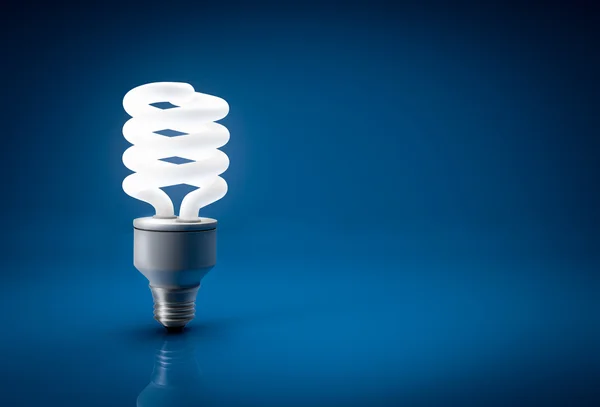 Lâmpada de poupança de energia brilhante sobre fundo azul — Fotografia de Stock