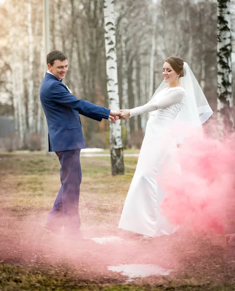 Bruid en bruidegom dansen in het park op rode rook — Stockfoto