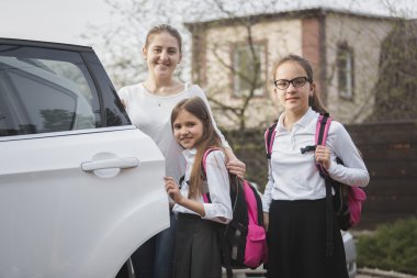 Mutlu anne ve iki kız okul çantaları arabaya poz ile
