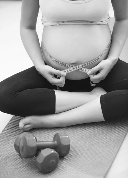 Foto em preto e branco da mulher grávida sentada em um tapete de fitness — Fotografia de Stock