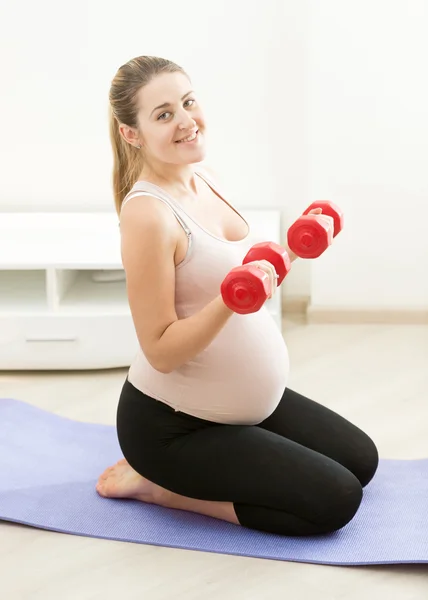 Donna incinta seduta su tappetino ed esercizio fisico con pesi — Foto Stock