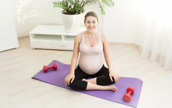 Donna incinta in posa sul tappeto fitness in soggiorno — Foto Stock