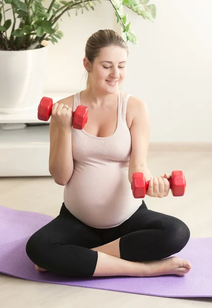 Zwangere vrouw oefenen met rode gewichten op fitness mat op hom — Stockfoto