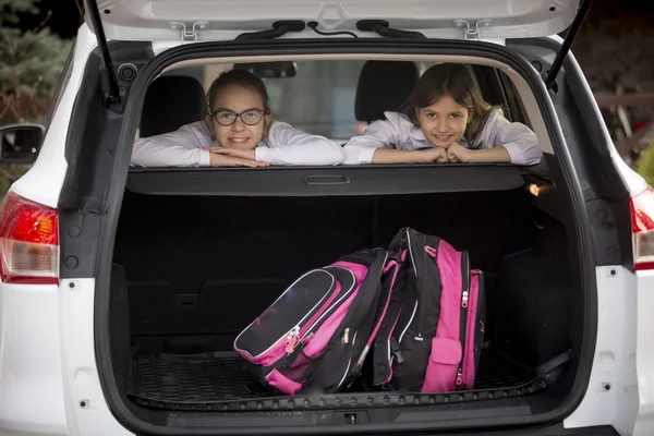 Twee lachende schoolmeisjes op zoek via open auto kofferbak — Stockfoto