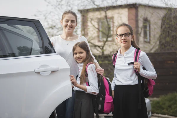 Gelukkig moeder en twee meisjes met schooltassen poseren op de auto — Stockfoto