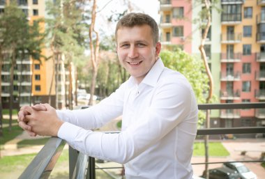 Genç adam güneşli gün balkonda poz Beyaz gömlekli gülümseyen