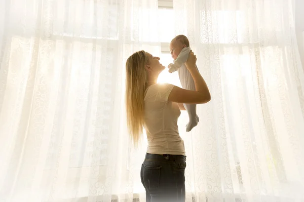 Giovane madre che tiene il suo bambino alla finestra nella luminosa giornata di sole — Foto Stock