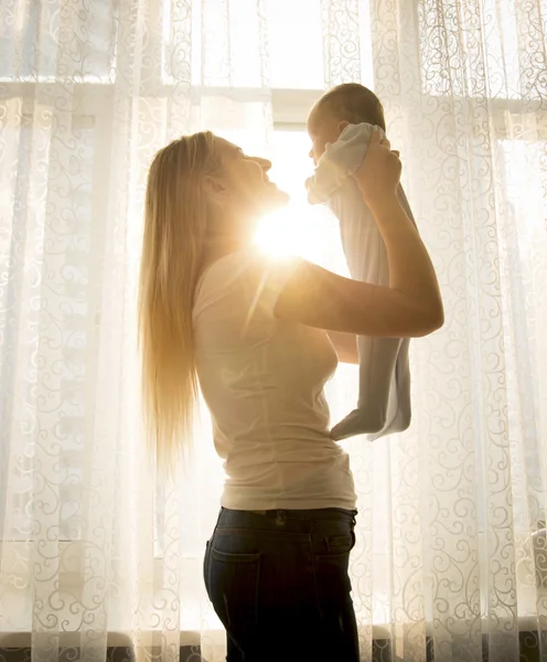 Silhouette photo contre le soleil de la jeune mère jouant avec bébé un — Photo